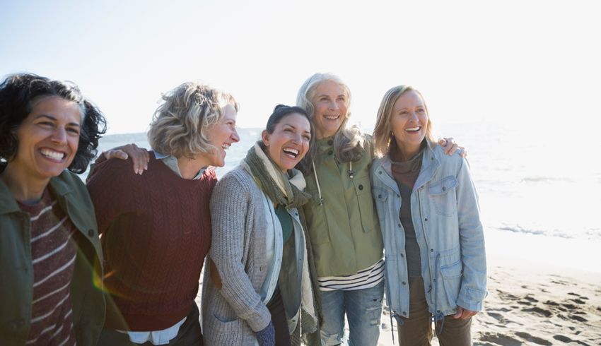Five woman stand shoulder-to-shoulder with one arm around the other.